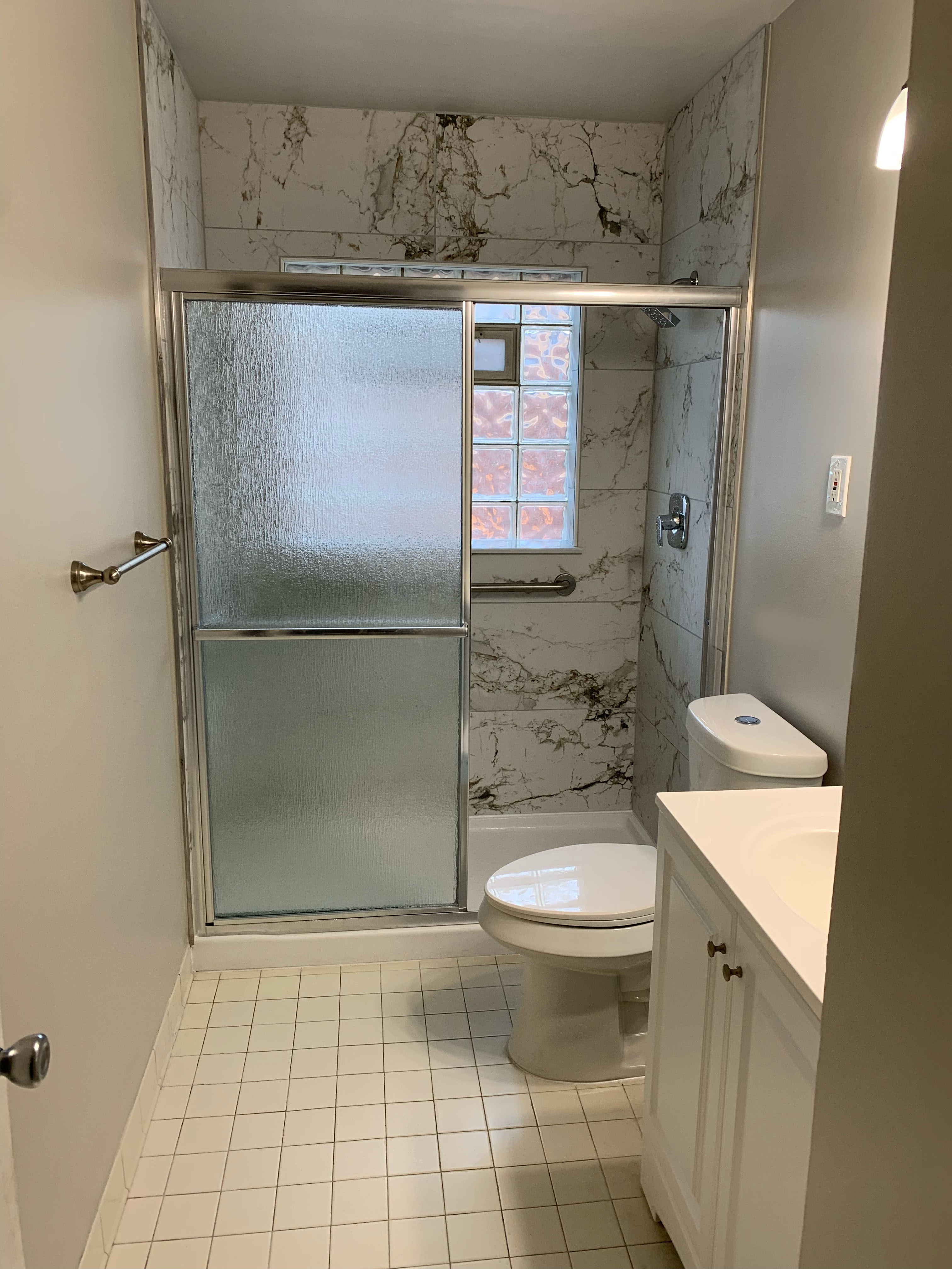 Tub-to-shower conversion bathroom remodelwith accessible walk-in shower, safety grab bar, sliding glass panels, and marble-look tile walls